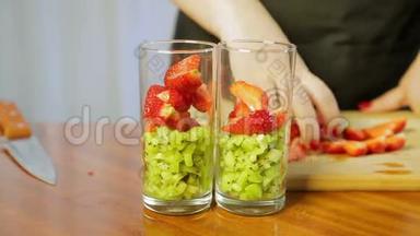 一个女人把碎奇异果片和成熟草莓放进玻璃杯里