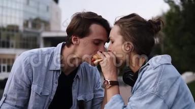 一对漂亮的年轻夫妇<strong>一起吃饭</strong>。 从两边<strong>一起</strong>吃汉堡包。 傍晚时分，公园侧