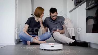男人和<strong>女人坐在</strong>家里<strong>的地板上</strong>，试图打开智能手机中使用应用程序<strong>的</strong>机器人吸尘器
