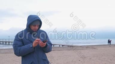 穿着蓝色羽绒服的人在海边的沙滩上打手机<strong>留言</strong>。