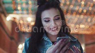 旋转观看美丽的黑发女孩使用她的手机和微笑的屏幕在俱乐部入口处。 夜总会