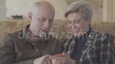 一对成年夫妇坐在<strong>大沙发</strong>上，秃头的女人在手机上为他的灰短老头拍照