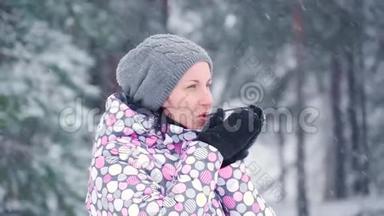 一个女孩站在寒冷的森林或公园里，在一个下雪的冬天。 一位女游客从杯子里喝热茶。 旅游业和旅游业