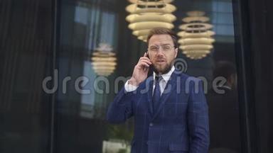 成功的商人戴着圆眼镜<strong>赢得</strong>了胡须，在电话里交谈，看着他的手表，手表上挂着玻璃墙。