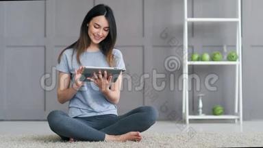 年轻快乐<strong>的女人坐在地板上</strong>，在家里使用平板电脑