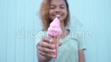 微笑着的黑人女孩在蓝墙背景下缓慢地吃粉色融化的冰淇淋
