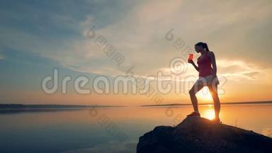 一个女运动员在<strong>湖边</strong>喝水。 一个女孩在<strong>湖边的</strong>日落背景上从一个特殊<strong>的</strong>瓶子里喝酒。