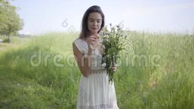 肖像可爱的年轻女孩，黑发，穿着一件白色的夏季时尚长裙，站在田野上。 休闲
