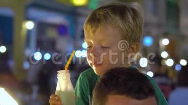在泰国的一个夜市上，小男孩坐在父亲的脖子上`着新鲜的果汁。 泰国菜的概念。 亚洲