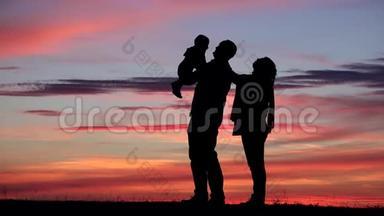 父母和婴儿剪影和夕阳红的天空，父亲养育孩子，嬉戏
