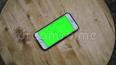 智能手机用铬键旋转，绿色屏幕。 阿尔法视频，木制背景上的手机。 模拟视频