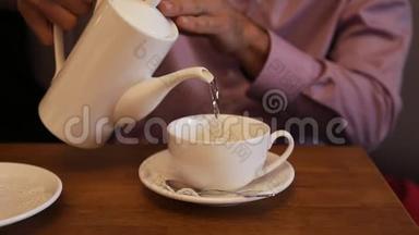 男人用一个白茶壶把<strong>热水倒</strong>入木桌上的白杯里泡茶