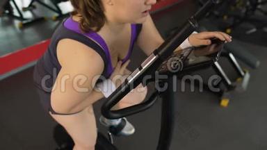 疲惫的超重妇女坐在固定的自行车上，<strong>呼吸困难</strong>
