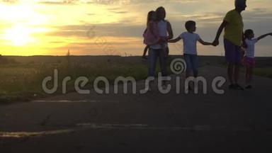 幸福的爸爸和妈妈带着三个孩子在日落时在农村上路。 幸福的家庭在大自然中玩得很开心。 旅费