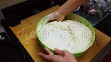 年轻的女人在家里用绿色的碗揉面包面团。 隔离或隔离的人们<strong>自己做</strong>面包的概念