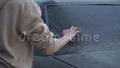 一个年轻的女人用手指在一辆脏车上写字`请帮我洗一下。`个恶作剧的女孩超过了车主。 汽车上覆盖着