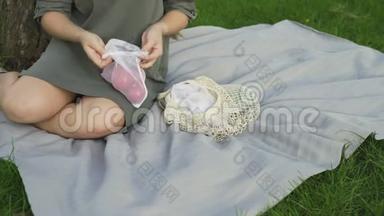 无法辨认的女人坐在毯子上，在夏天的公园里从棉网购物袋里拿番茄。 零废物