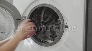 女用手拿着洗衣机上的绿色衣服。 去装洗衣机。 把衣服装进洗衣机。 负荷