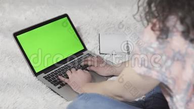 这位年轻女子使用笔记本<strong>电脑</strong>和键盘打字，工作场所在家里。 带<strong>绿</strong>色<strong>屏幕</strong>的笔记本<strong>电脑</strong>