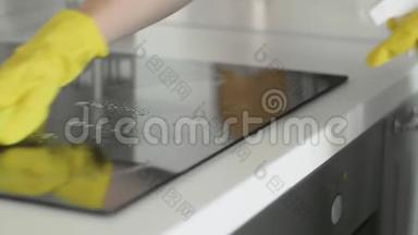 用除脂剂喷雾剂和黄色抹布清洗厨房的烹饪面板，由一位戴黄色橡胶手套的女士清洗。