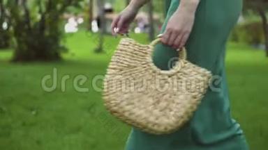 在夏季公园里，一个年轻的女人用手工制作的时尚草包走着。 <strong>环保袋</strong>。