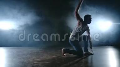 现代芭蕾，一个人从<strong>舞台上的</strong>一个坐姿，<strong>在</strong>烟雾中<strong>的</strong>一个黑暗<strong>的舞台上</strong>，旋转着跳回