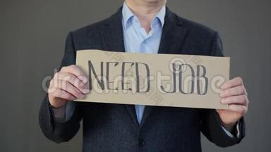 失业商人在灰色背景上持有需要工作标志的海报。 找工作的失业经理