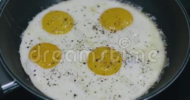 在黑金属锅里煮四个煎蛋. 煎锅中四个鸡蛋的早餐食品准备。 上景。