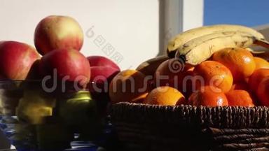 阳<strong>台桌</strong>上的橘子、香蕉和苹果，阳光明媚的天气，细节，柳条和玻璃碗