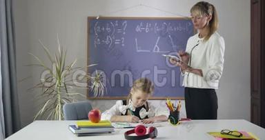 漂亮的高加索女孩在练习本中画画，作为成人私人教师在平板电脑中搜索任务。 儿童就读