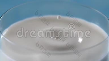 牛奶在缓慢的运动中滴到满杯，液体在缓慢的运动中大镜头，桌面视频，滴