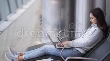 年轻女子坐在候机室，用笔记本电脑在机场工作