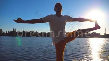 站在<strong>瑜伽馆</strong>前的年轻人在湖边的木制码头摆姿势。 运动员在大自然中单腿平衡。 体育界的家伙