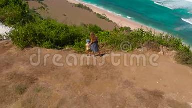 一名年轻女子和她的儿子在巴厘岛的一个偏僻的海滩上，在空中拍摄了一个缓慢的镜头-尼扬-。 站立站立