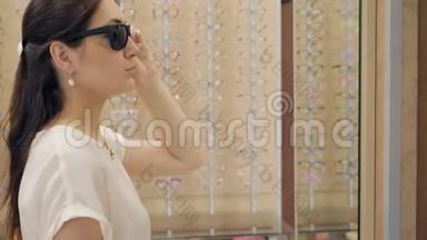 一家眼镜店的女人在镜子前戴太阳镜