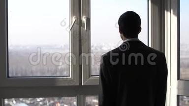 年轻的成功商人站在窗前眺望城市的远方。 慢动作