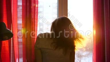 清晨站在窗边的女孩拉开窗帘.. 太阳`光线穿过玻璃，