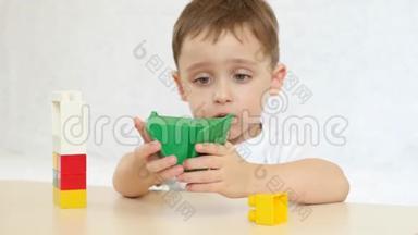 <strong>一个</strong>孩子正在用彩色积木玩耍，坐在白色背景的桌子旁。 孩子和玩具。 聚焦相机的<strong>目标</strong>是