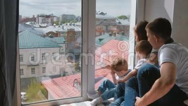 家庭妈妈，爸爸和两个双胞胎兄弟蹒跚学步的孩子看着窗外的城市。