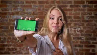 年轻的白种人金发女孩显示智能<strong>手机屏</strong>幕，绿色屏幕，推荐应用程序，如标志，肖像，砖块